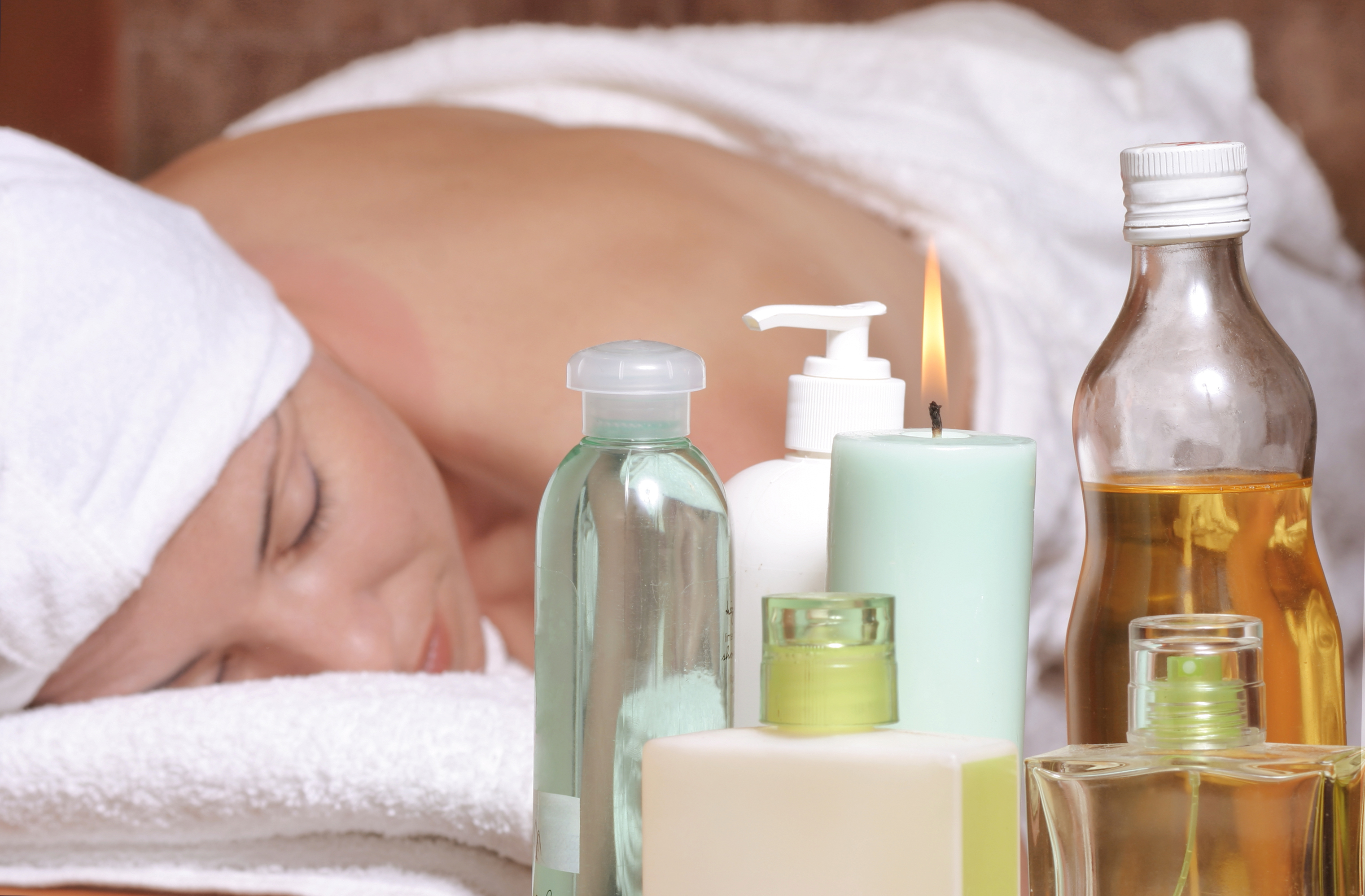 Woman in white towels on massage table with oils, essential oils, candles, scents.